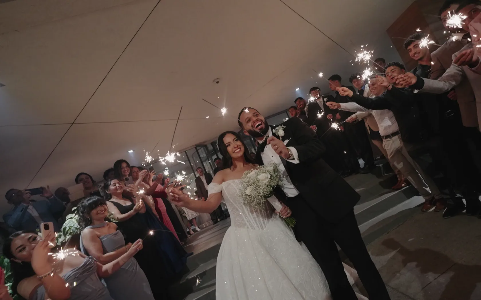 Kiro & Rana walking out through a tunnel of sparklers, both beaming