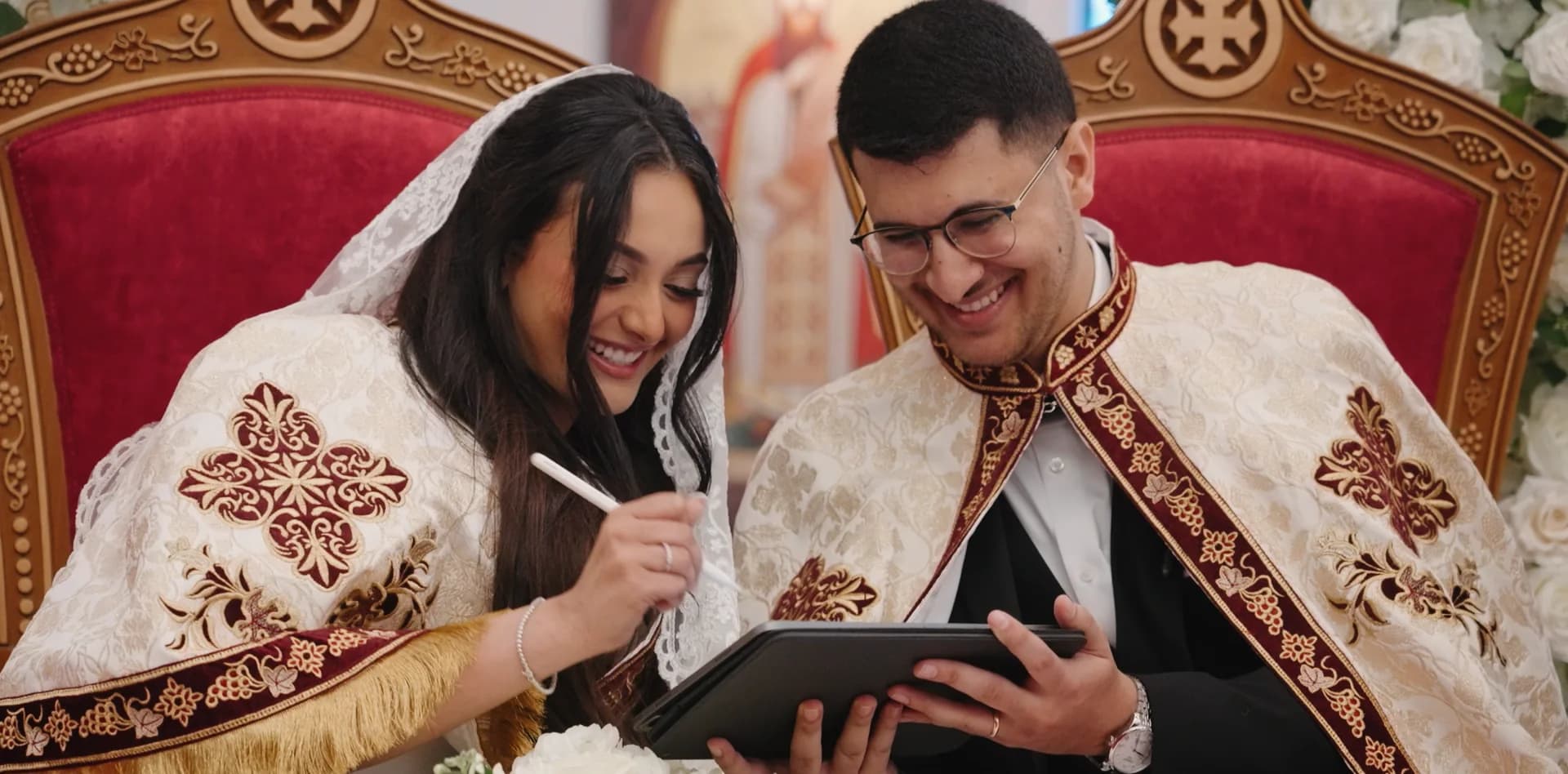 A Coptic Orthodox bride and groom in ceremonial robes, smiling as they sign during the ceremony