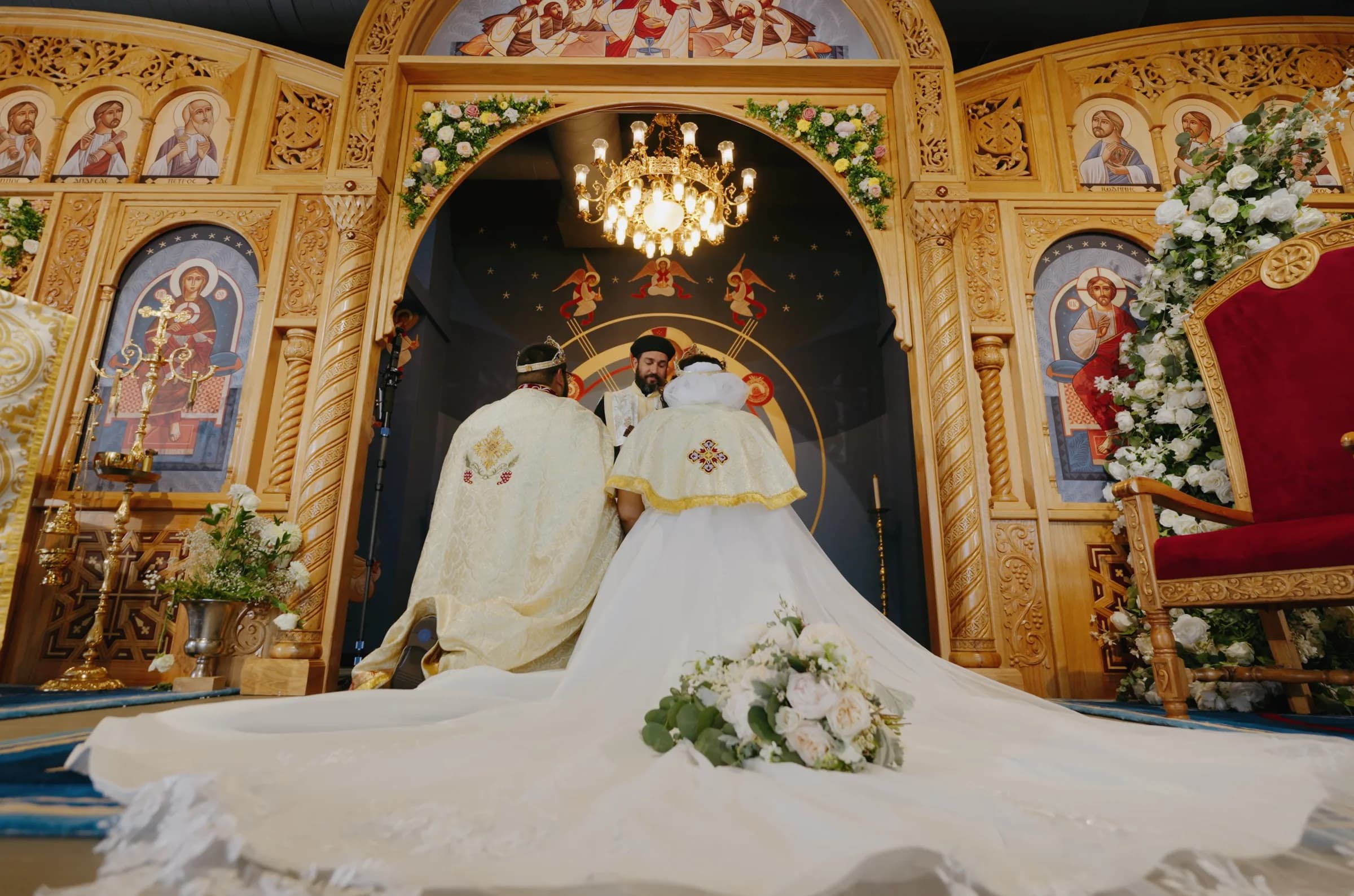 A crowned couple stand before the altar of a Coptic Orthodox church, the bride's dress spread behind her.