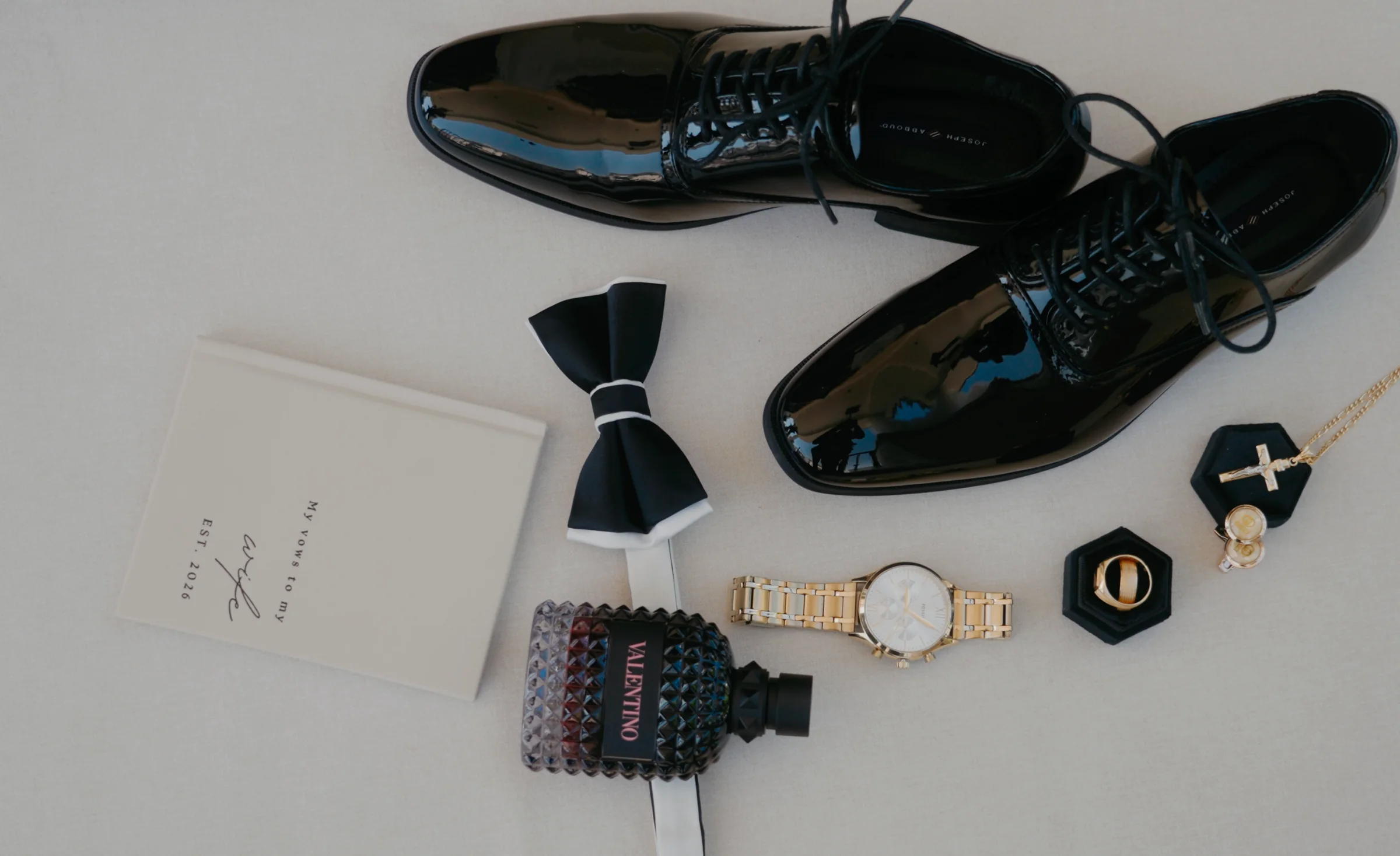 Groom's shoes, bow tie, watch, ring and a cross laid out together.