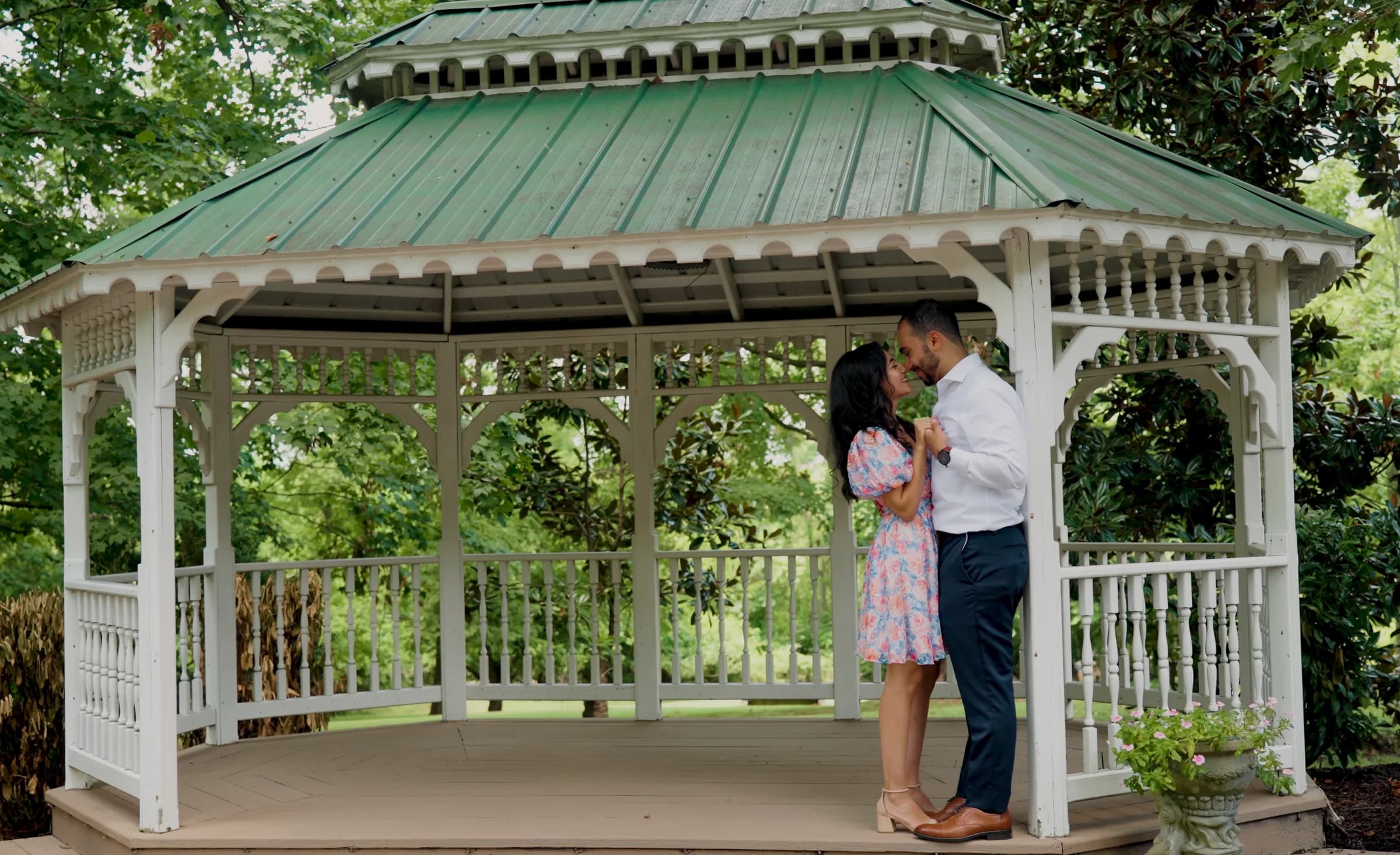 A couple stand forehead to forehead inside a garden gazebo.