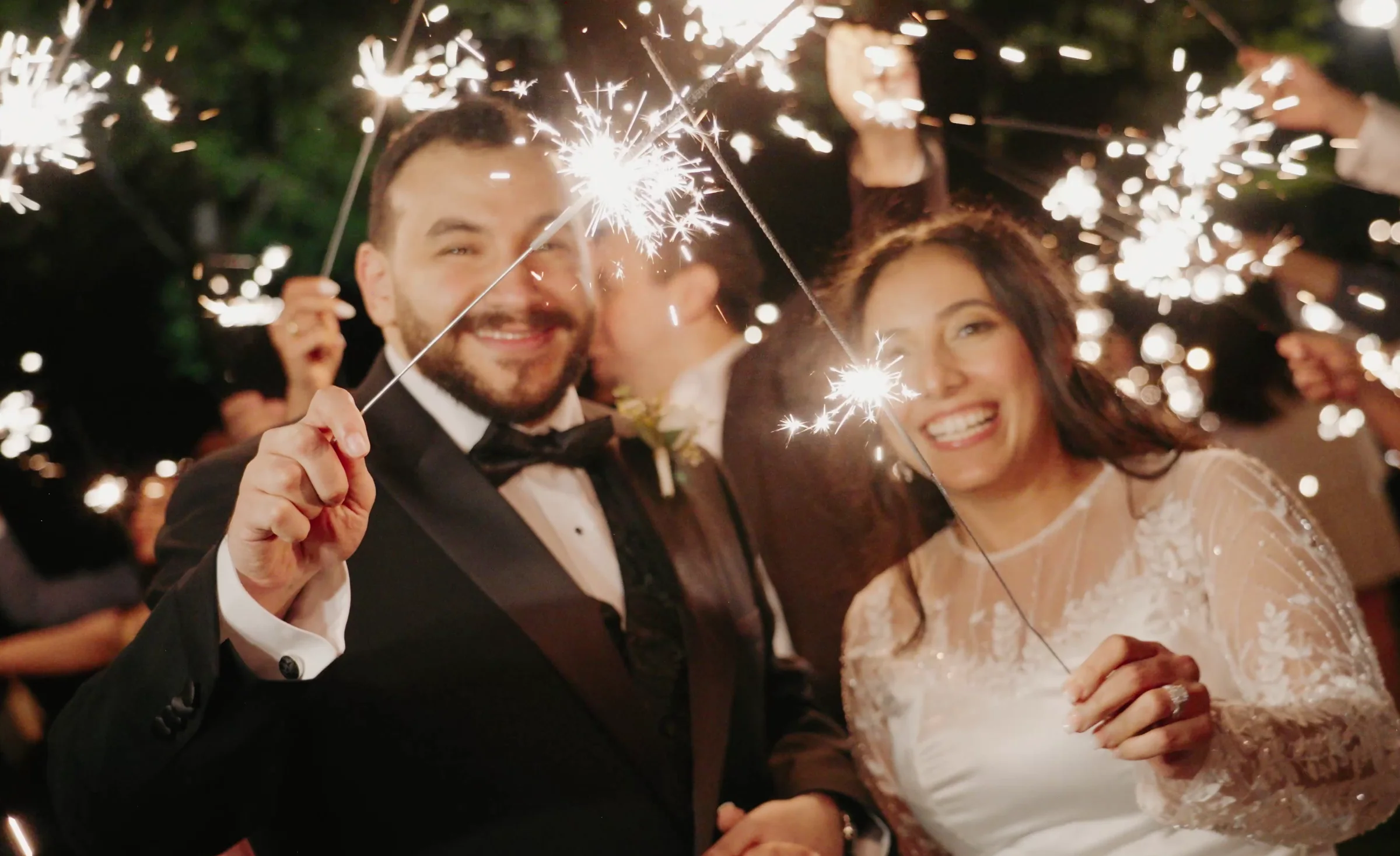 A couple walk out through raised sparklers, both laughing.