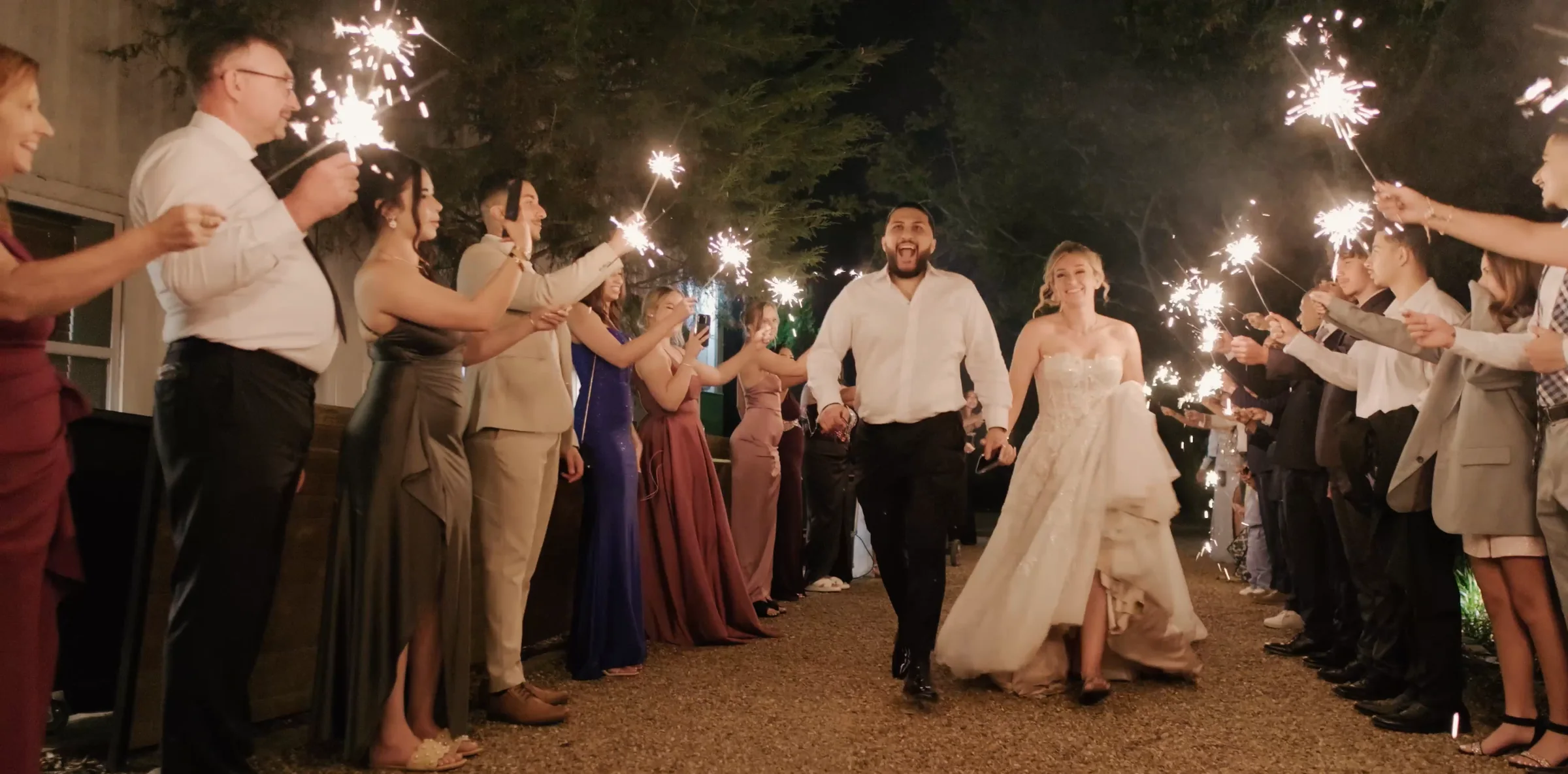 A couple run out through a long tunnel of sparklers held by guests.