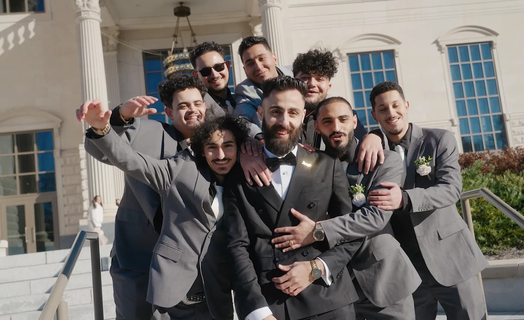 A group of groomsmen crowd around the groom and grin at the camera.