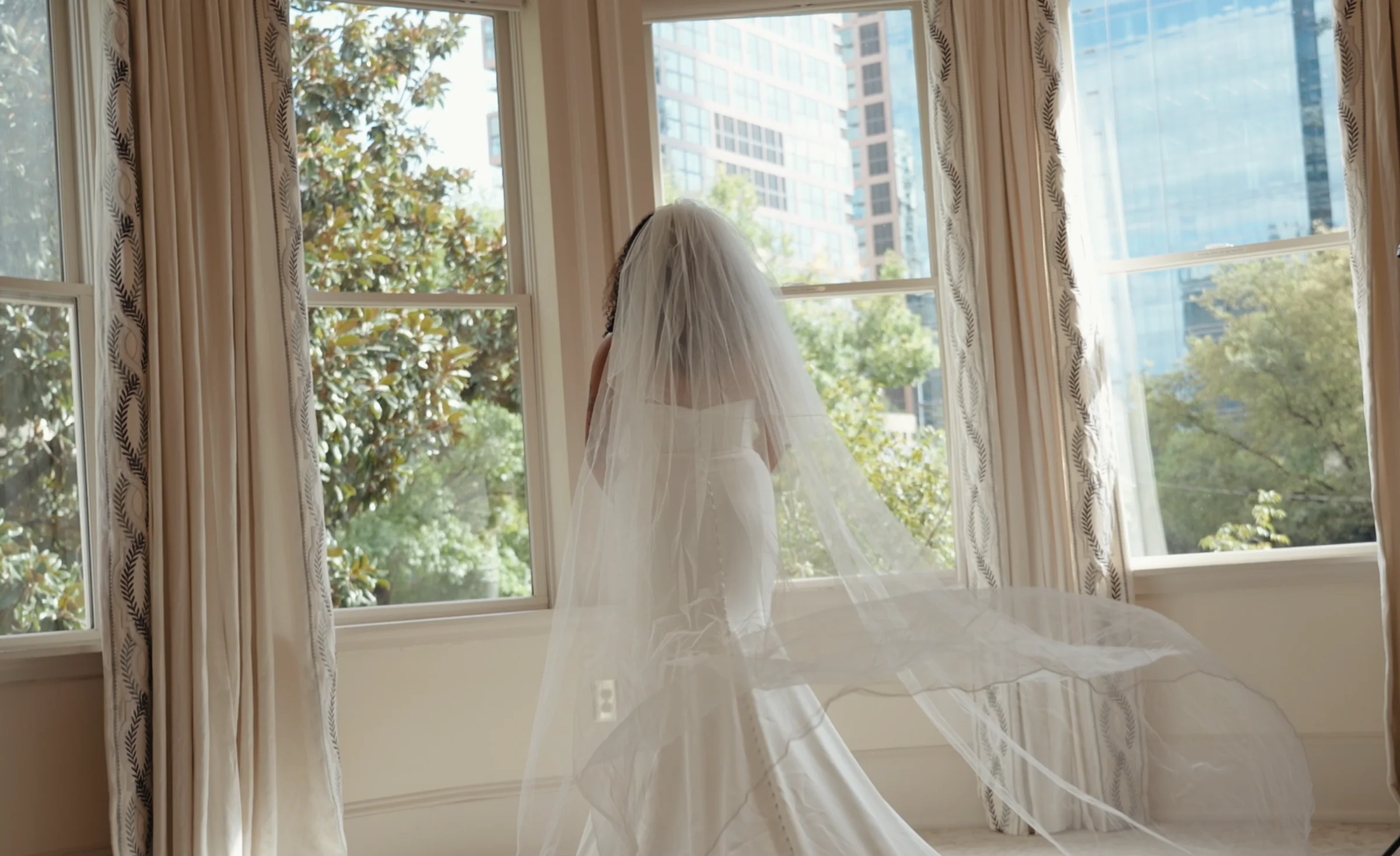 A bride alone at the window, her veil falling to the floor behind her