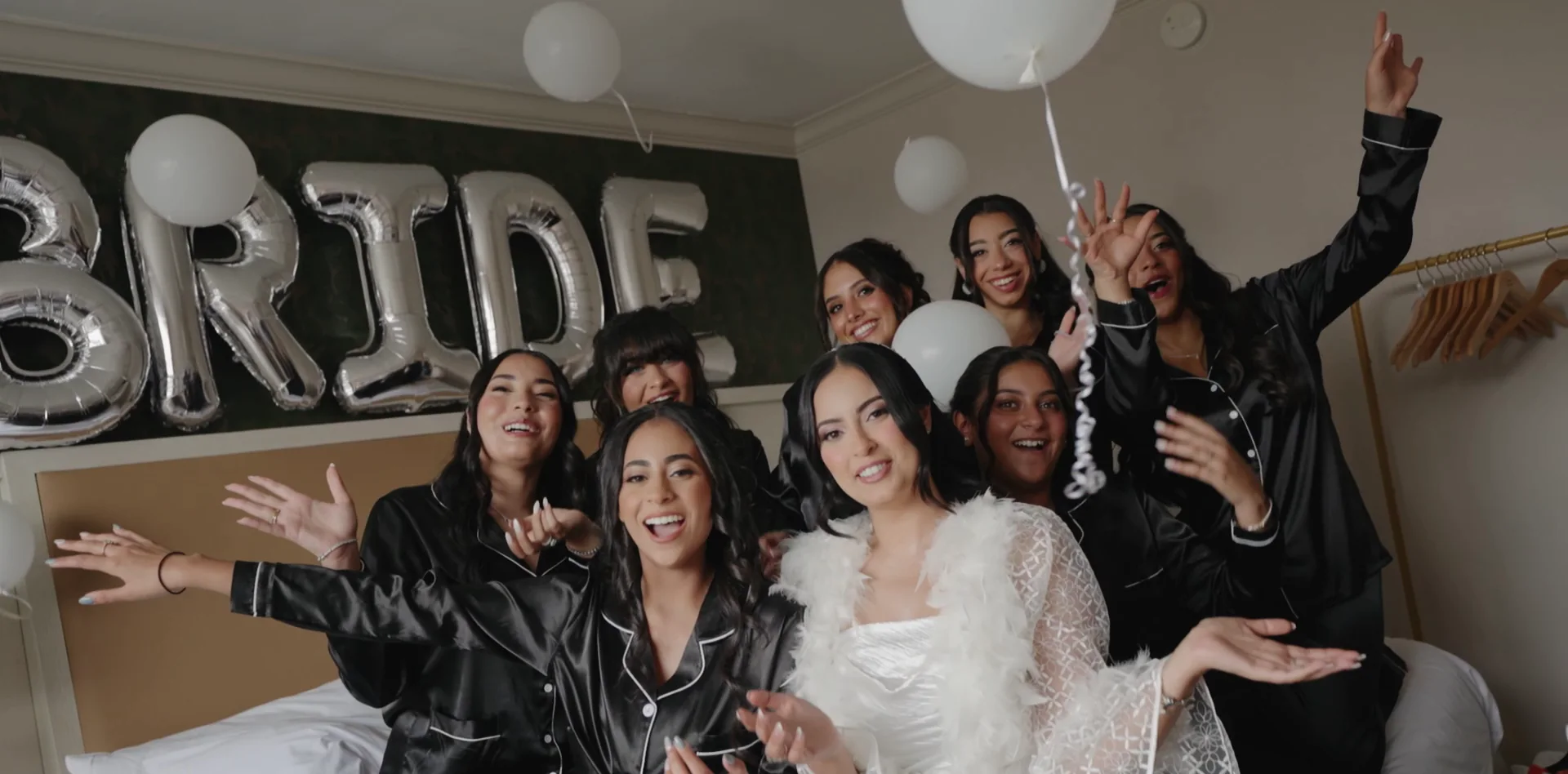 A bride and her bridesmaids celebrate together on a bed in matching pyjamas.