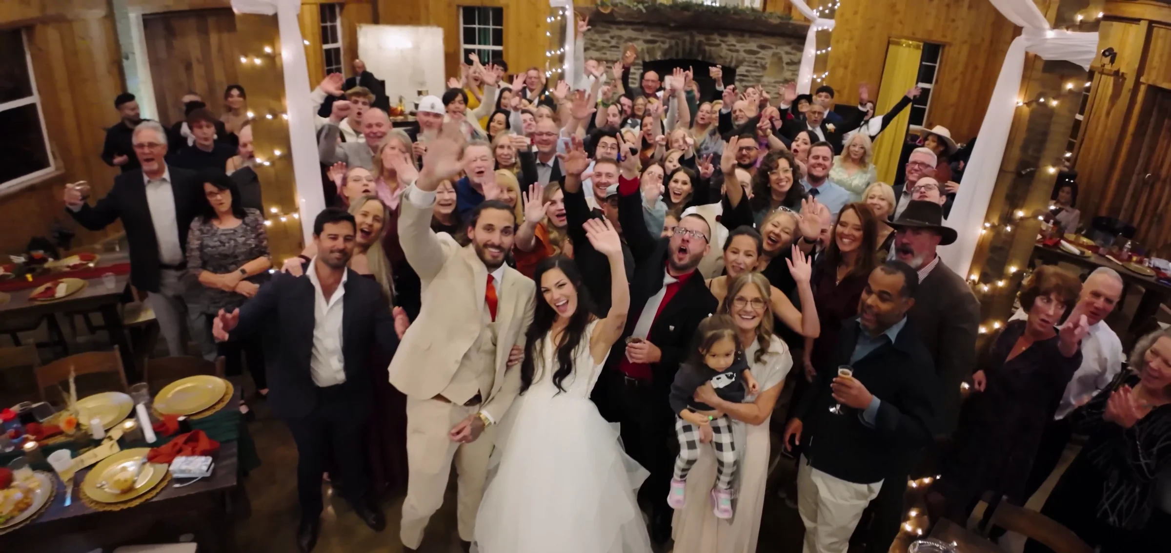 A full reception room cheers around the couple standing at the centre.