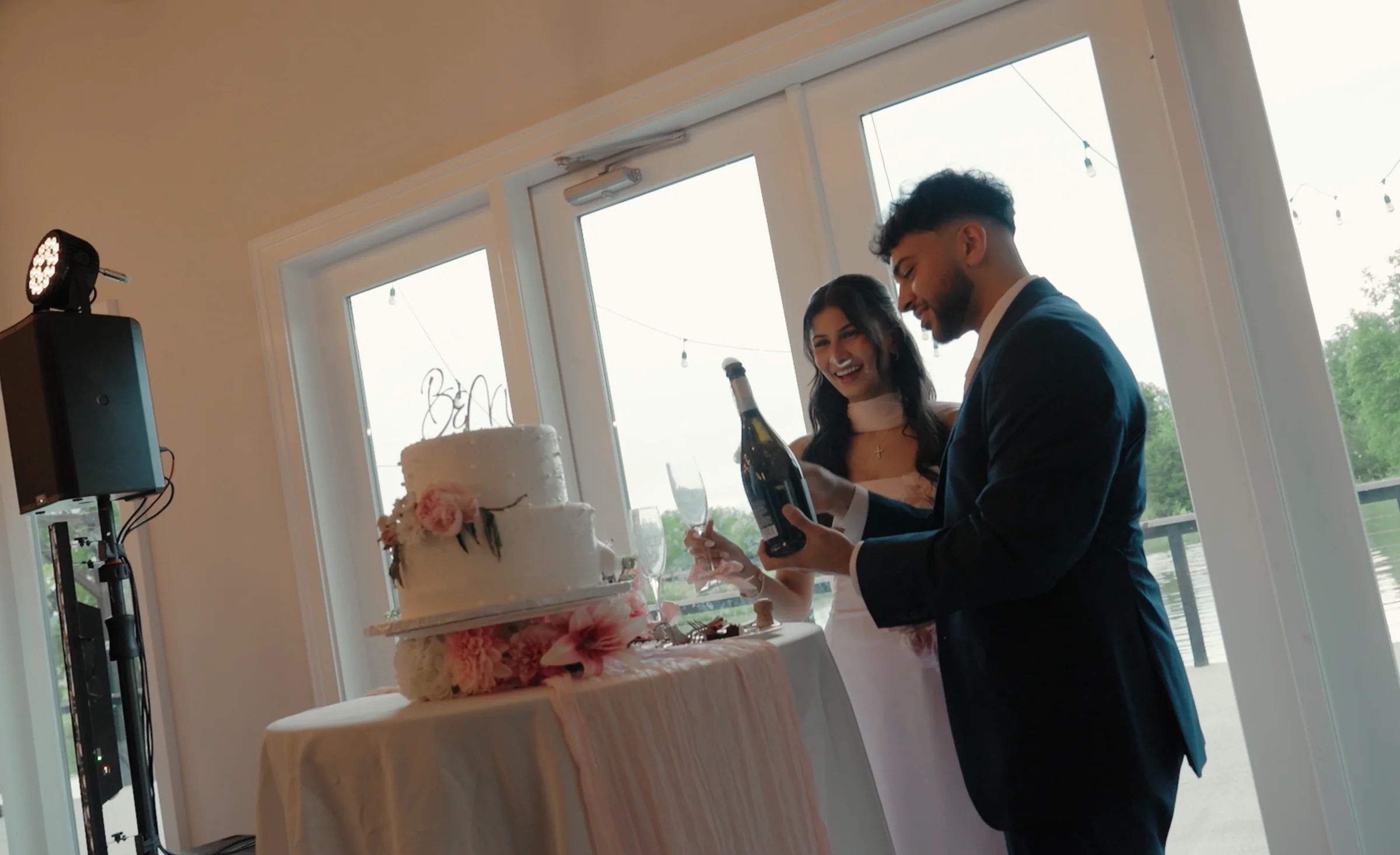 A couple laugh together with a champagne bottle beside their cake.